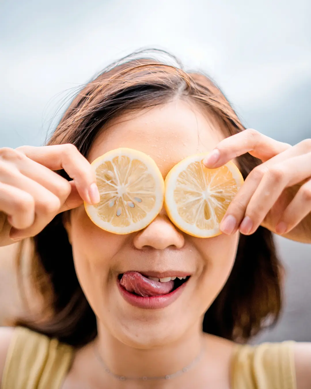 A woman playfully holding lemon slices over her eyes